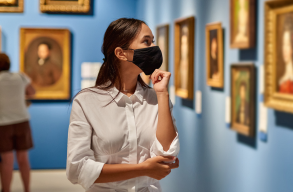 Personne portant un masque, observant des œuvres encadrées dans une salle de musée.