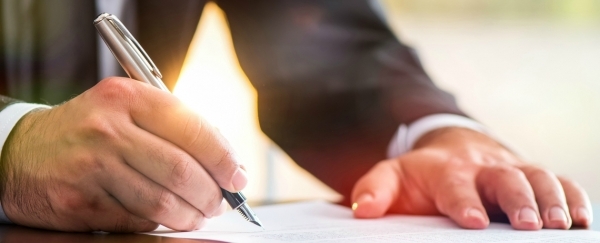 Main tenant un stylo et signant un document posé sur une table.