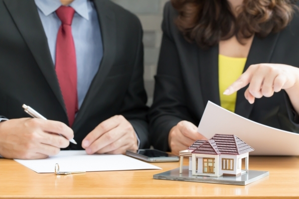 eux personnes examinant des documents sur une table, avec une maquette de maison au premier plan.