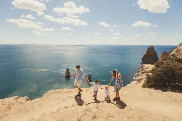 Quatre personnes marchant ensemble sur un sentier rocheux en bord de mer, avec l’océan et des falaises en arrière‑plan.