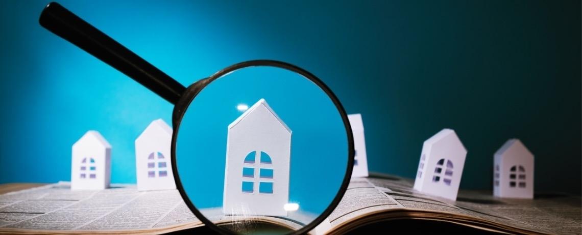 Illustration d'une loupe posée sur un livre ouvert met en évidence une petite maison miniature blanche, entourée d’autres maisons similaires, sur un fond bleu.