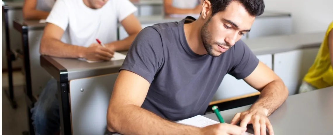 Personnes assises à une table, écrivant sur des feuilles dans une salle de classe.