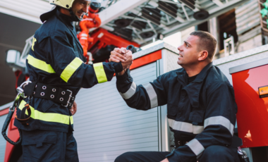 Deux pompiers se serrant la main devant un véhicule de secours.