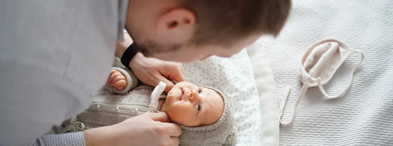 Un parent se penchant au‑dessus de son nourrisson allongé sur un lit, ajustant ses vêtements