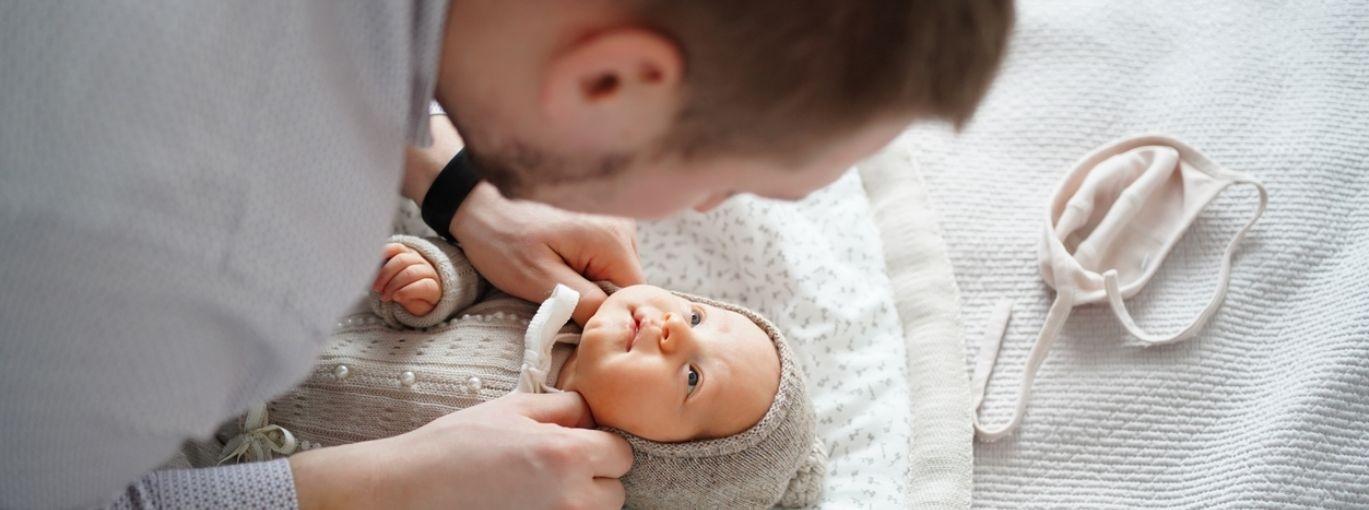 Un parent se penchant au‑dessus de son nourrisson allongé sur un lit, ajustant ses vêtements