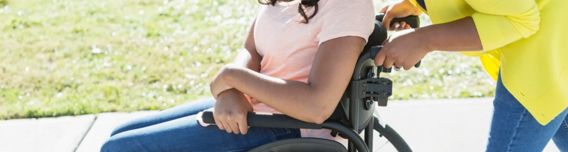 Personne assise dans un fauteuil roulant pendant qu’une autre personne pousse le fauteuil en extérieur