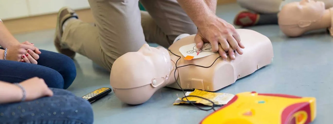 Une personne effectue des compressions thoraciques sur un mannequin de secourisme lors d’un exercice de gestes de premiers secours, avec du matériel de formation visible autour.