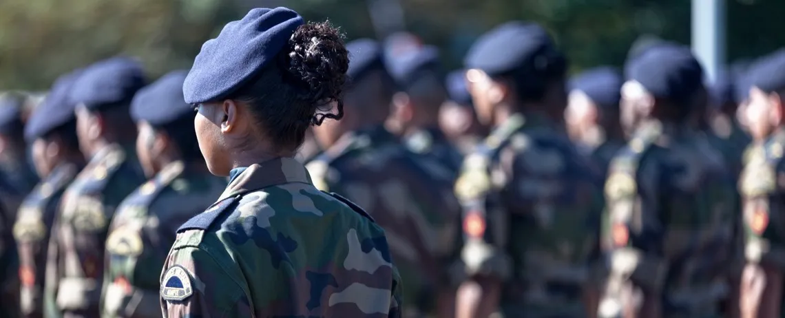 Personnes en tenue militaire alignées en formation, vues de dos, lors d’un rassemblement en extérieur.