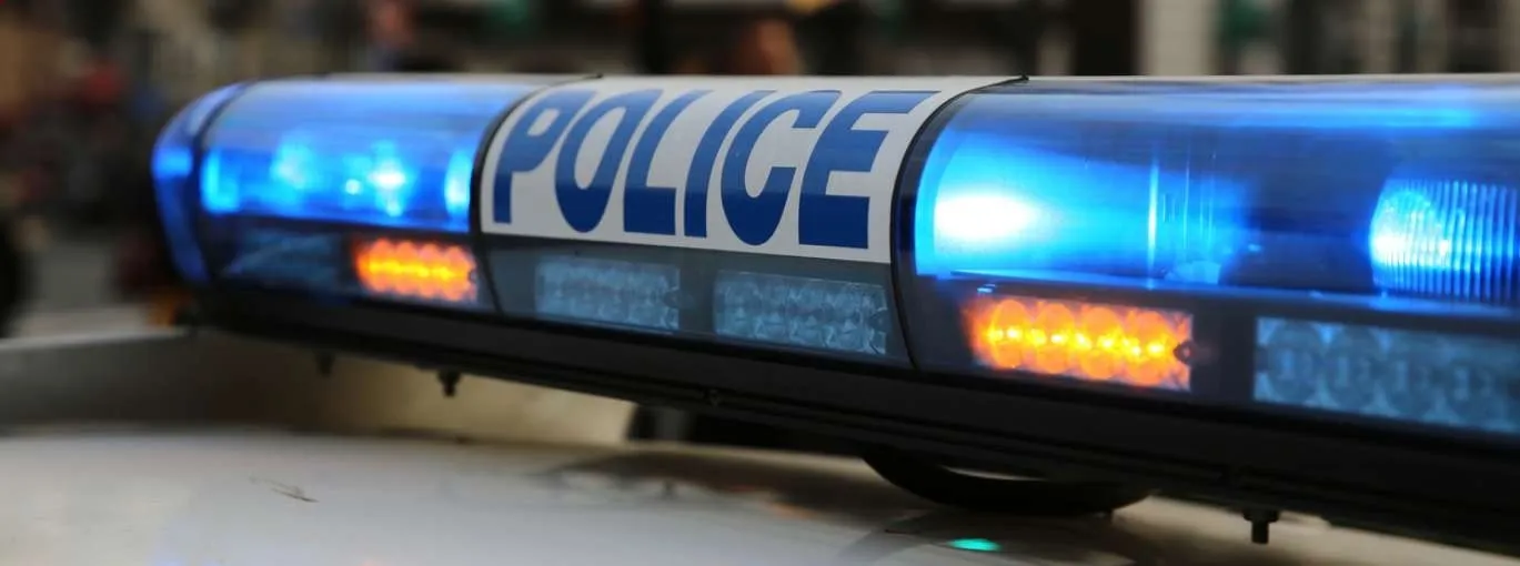 Un gyrophare de véhicule de police allumé, avec l’inscription « POLICE » visible, sur fond urbain flou.