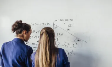deux femmes de dos devant faisant des calculs sur tableau blanc