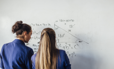 deux femmes de dos devant faisant des calculs sur tableau blanc