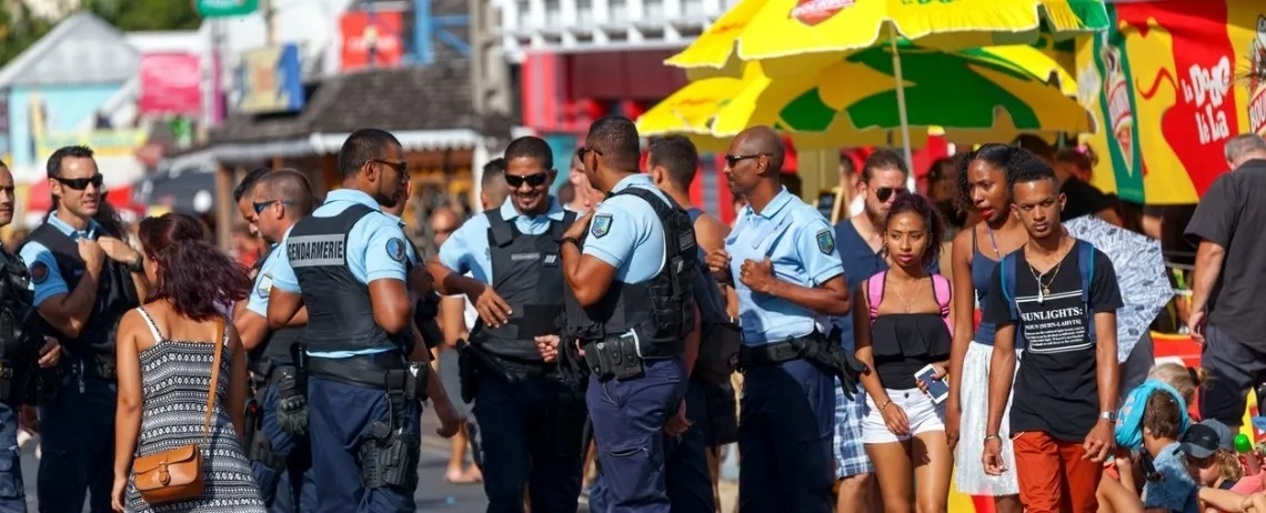 Des gendarmes en tenue sont présents au milieu d’une foule dans un espace public animé, avec des stands et des passants en arrière-plan.