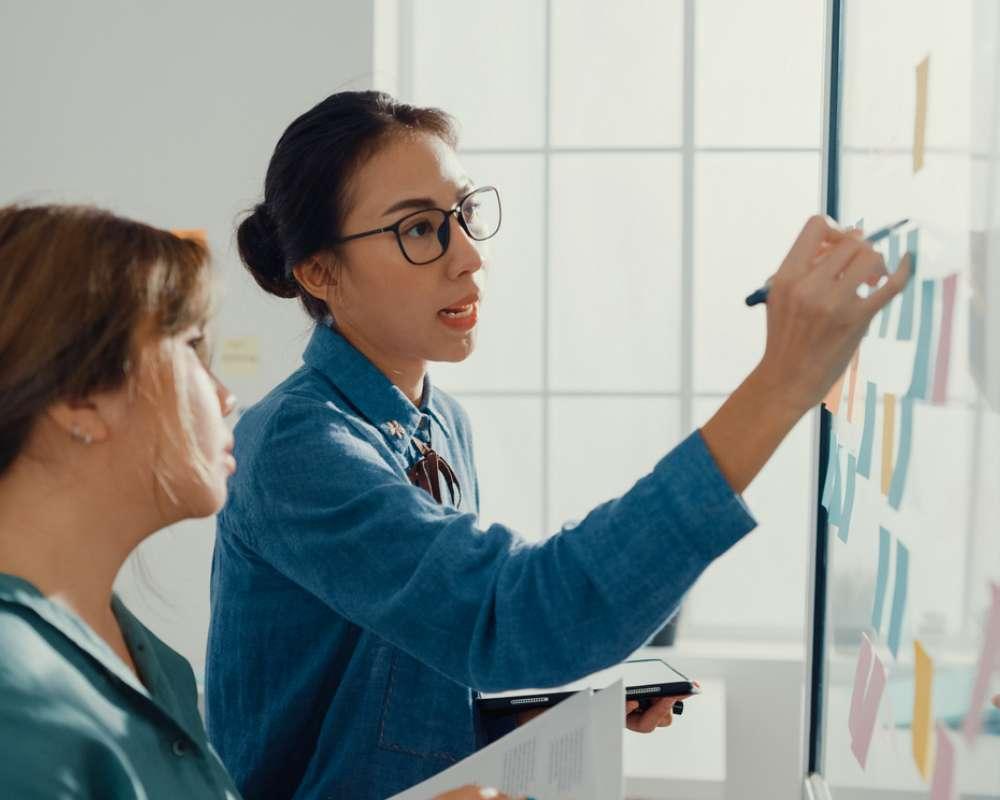 deux salariées écrivent le process de projet sur un tableau blanc