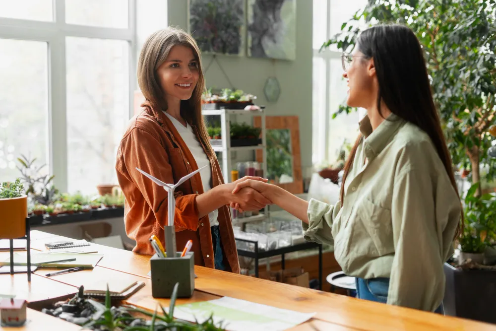 deux femmes se serrent la main dans un bureau avec de la nature